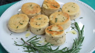 7 mini foccacia biscuits, served on a white plate garnished with rosemary, thyme, and a drizzling of olive oil.