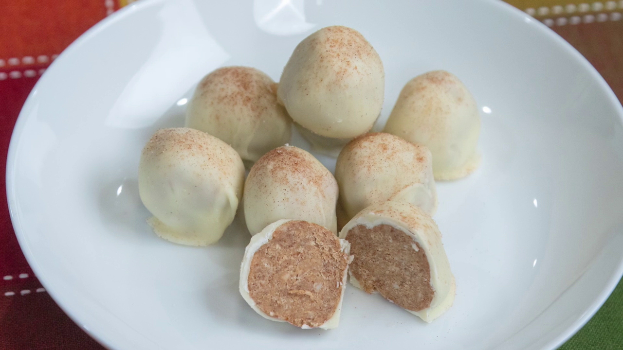 The finished White Chocolate Pumpkin Truffles, served on a white plate and topped with cinnamon sugar. One of the truffles is cut in half to show the filling.