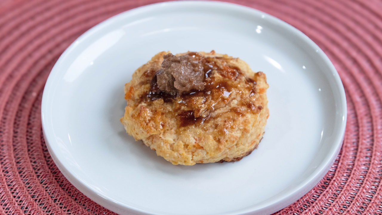 One of the Sweet Potato Biscuits, topped with Maple Butter, served on a white plate and red placemat.