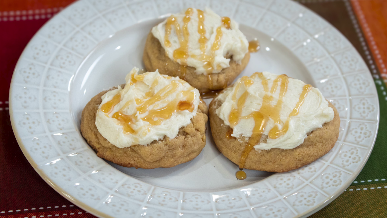 Three cornbread cookies topped with frosting and a drizzle of honey, served on a white plate.